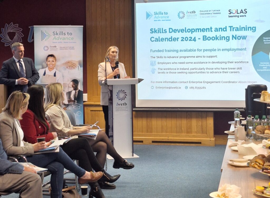 A woman standing at an LWETB podium giving a presentation. A presentation is shown on the screen behind.